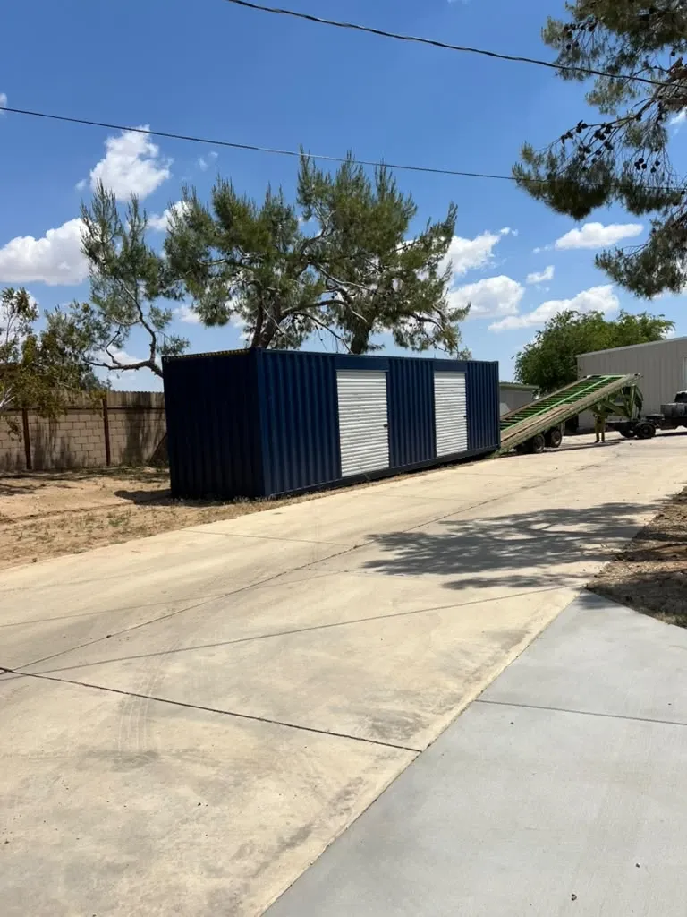A 40 ft container with two roll-up doors sliding off a tilt trailer onto a driveway
